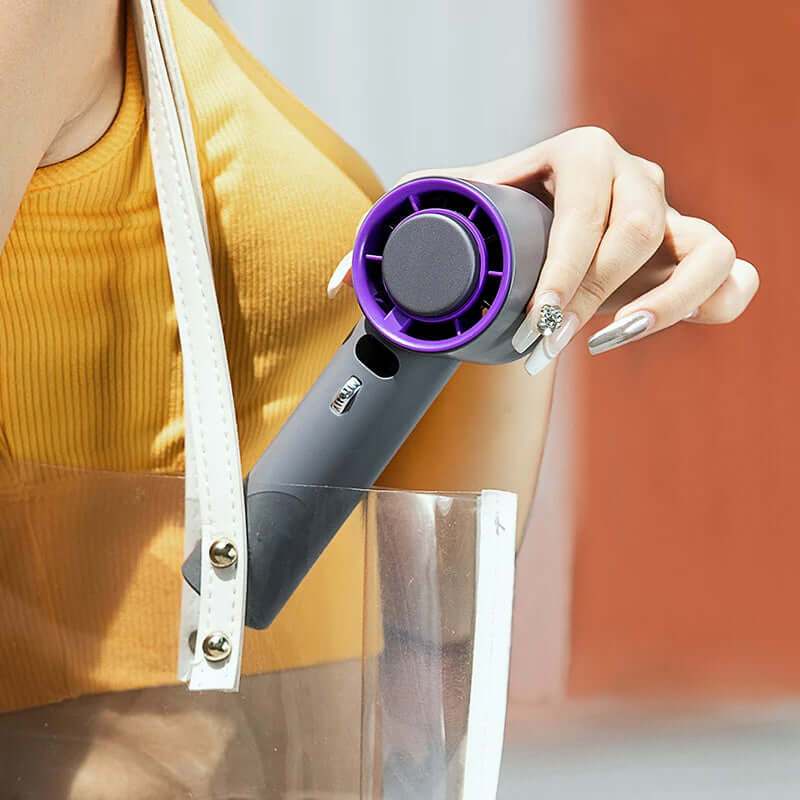 Portable handheld turbo fan being held in a clear tote bag, showcasing its compact design and stylish color.